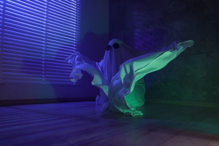 Creepy ghost. Woman covered with sheet near window in blue light