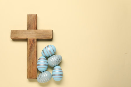 Wooden cross and painted Easter eggs on beige background, flat lay. Space for textの写真素材