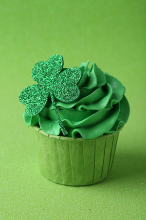 St. Patrick's day party. Tasty cupcake with clover leaf topper and cream on green background,...