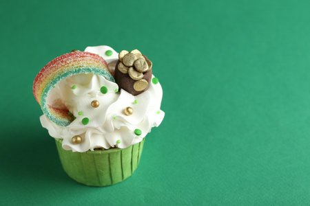 St. Patrick's day party. Tasty cupcake with sour rainbow belt and pot of gold toppers on green background, closeup. Space for textの写真素材
