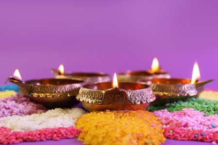 Diwali celebration. Diya lamps and colorful rangoli on purple background, closeup