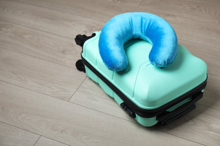 Turquoise travel pillow and suitcase on floor, space for textの写真素材