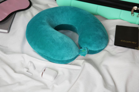 Turquoise travel pillow, suitcase, passport, sleep mask and earphones on bedの写真素材