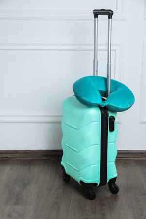 Turquoise travel pillow on suitcase near white wall indoorsの写真素材