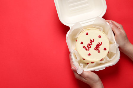 Woman holding takeaway box with bento cake at red table, top view. St. Valentine's day surpriseの写真素材