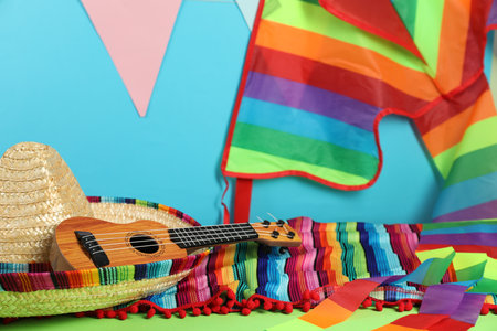 Mexican sombrero hat, poncho and ukulele on green table