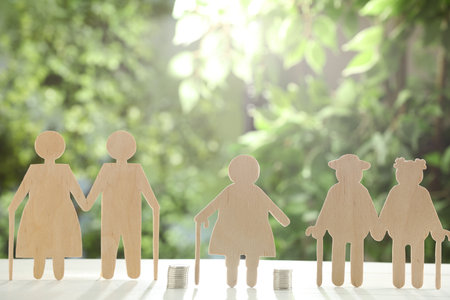 Pension savings. Figures of elderly people and coins on white table against blurred green backgroundの写真素材
