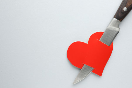 Broken heart. Red paper heart pierced with knife on white background, top view. Space for textの写真素材