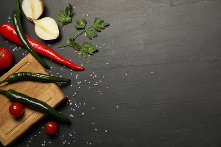 Cooking concept. Wooden cutting board and different products on black table, flat lay. Space for textの写真素材