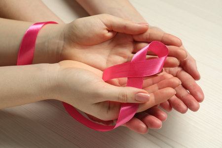 Women holding pink ribbon at white wooden table, closeup. Breast cancer awarenessの写真素材