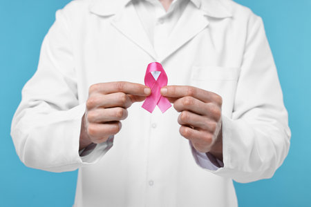 Mammologist giving pink ribbon on light blue background, closeup. Breast cancer awarenessの写真素材