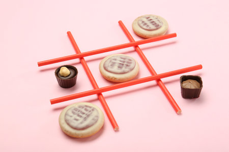 Tic tac toe game made with cookies and sweets on pink background