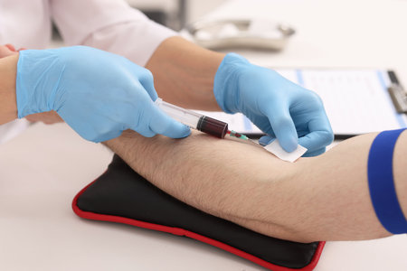 Doctor taking blood sample from patient with syringe at white table in hospital, closeupの写真素材