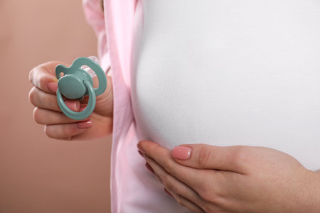 Pregnant woman holding pacifier on beige background, closeupの写真素材