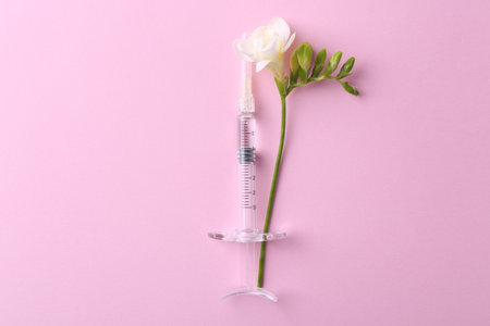 Cosmetology. Medical syringe and freesia flower on pink background, top viewの写真素材