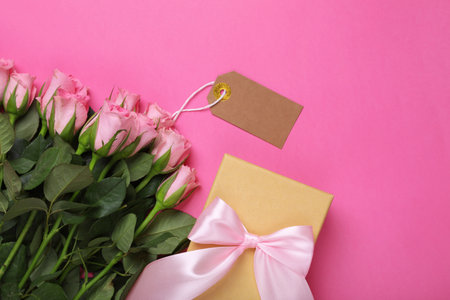 Happy Mother's day. Beautiful roses with tag and gift box on pink background, flat lay. Space for textの写真素材