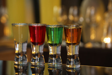 Different shooters in shot glasses on mirror surface against blurred background. Alcohol drink