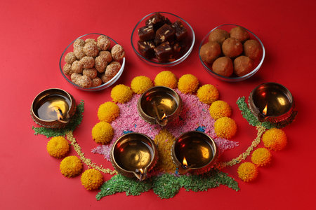 Happy Diwali. Composition with diya lamps, colorful rangoli, flowers and delicious Indian sweets on red table, above viewの写真素材