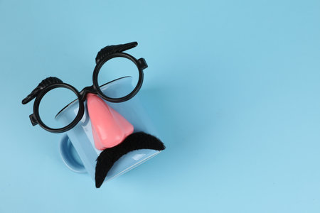 Man's face made of cup, fake mustache, nose and glasses on light blue background, top view. Space for textの写真素材