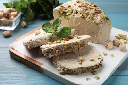 Pieces of tasty halva with pistachios and mint on light blue wooden table, closeup