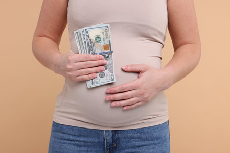 Surrogate mother. Pregnant woman with dollar banknotes on beige background, closeupの写真素材