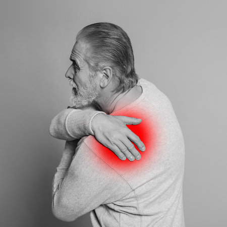 Senior man suffering from rheumatism on light background. Black and white effect with red accent in painful areaの写真素材