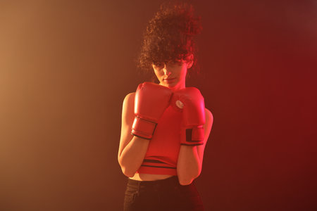Beautiful young woman with boxing gloves on color background in neon lights and smokeの写真素材