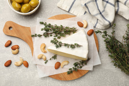 Piece of tasty camembert cheese, thyme, nuts and olives on gray textured table, flat layの写真素材