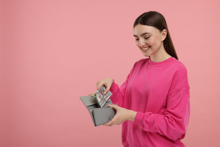 Happy woman putting money into wallet on pink background, space for textの写真素材