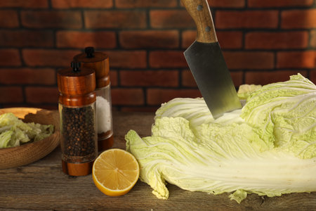 Fresh Chinese cabbage, knife, spices and lemon on wooden tableの写真素材