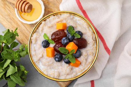 Delicious barley porridge with blueberries, pumpkin, dates and mint served with honey on light table, flat layの写真素材