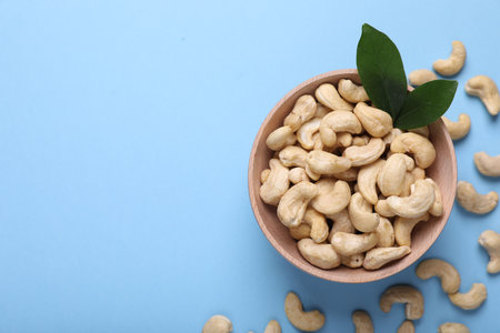 Many tasty cashew nuts and leaves on light blue background, top view. Space for textの写真素材