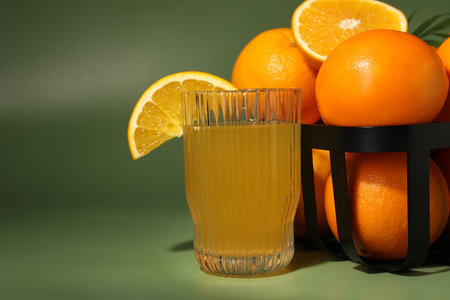 Fresh oranges in metal basket and glass of juice on green background, closeupの写真素材