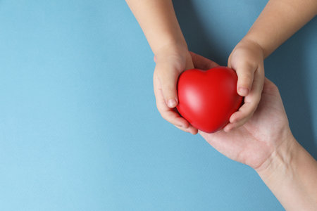 Mother and her child holding red decorative heart on light blue background, top view. Space for textの写真素材