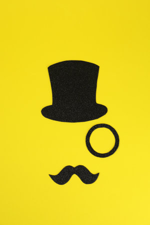 Man's face made of fake mustache, hat and monocle on yellow background, top viewの写真素材