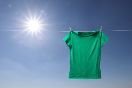 Green t-shirt drying on washing line against blue skyの素材