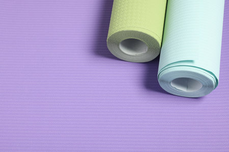 Two colorful wallpaper rolls on violet sample, above view. Space for text
