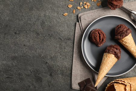 Chocolate ice cream scoops in wafer cones on gray textured table, flat lay. Space for textの写真素材