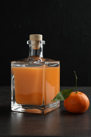 Delicious tangerine liqueur in glass bottle and fresh fruit on gray tableの写真素材