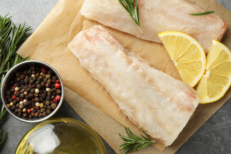 Fresh raw cod fillets, spices and lemon slices on gray table, flat lay