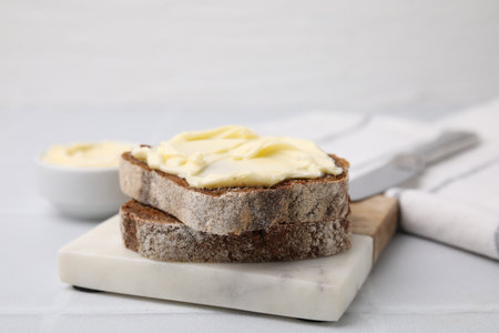 Slices of tasty bread with butter on white tiled table, closeup. Space for text