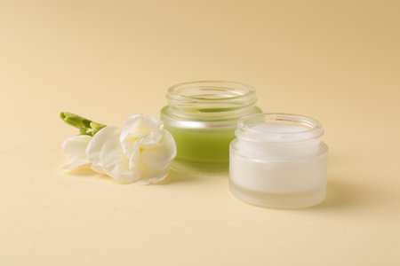 Moisturizing cream in open jars and freesia flower on beige background. Body care productsの写真素材
