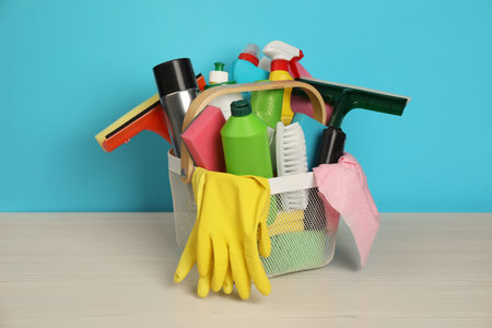 Different cleaning products in basket on wooden table against light blue backgroundの写真素材
