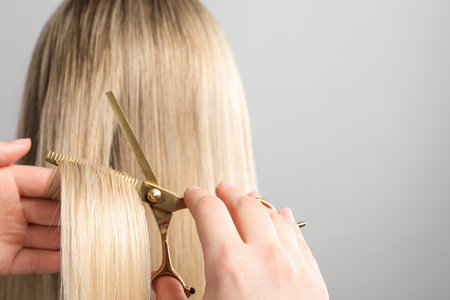 Hairdresser cutting client's hair with scissors on light gray background, closeup. Space for textの写真素材