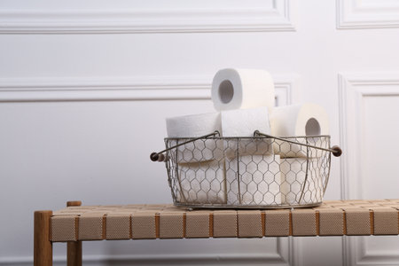 Soft toilet paper rolls in metal basket on wicker bench. Space for textの写真素材