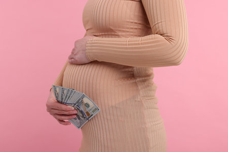 Surrogate mother. Pregnant woman with dollar banknotes on pink background, closeupの写真素材