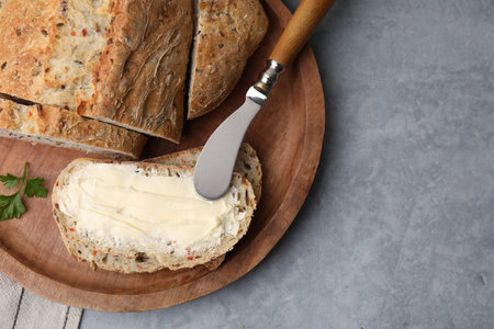 Tasty bread with butter and knife on gray textured table, top view. Space for text