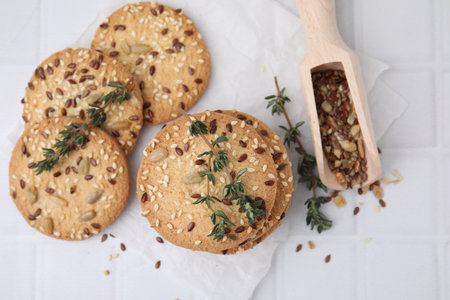 Cereal crackers with flax, sesame seeds, thyme and scoop on white tiled table, top viewの写真素材