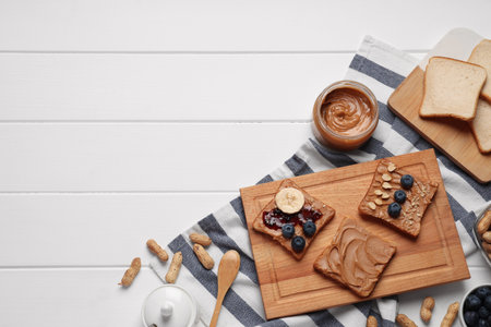 Different tasty toasts with nut butter and products on white wooden table, flat lay. Space for textの写真素材