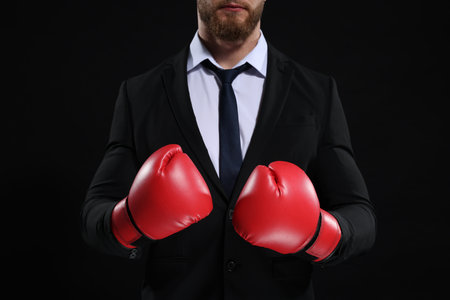 Businessman in suit wearing boxing gloves on black background, closeupの写真素材
